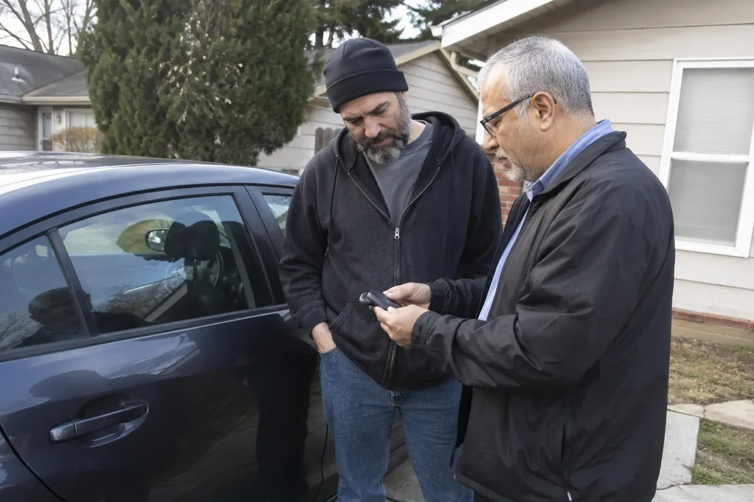 Two adults discussing a key fob beside a parked car. — Car Lockout Service, Mississauga